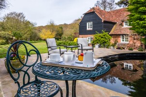 A garden setting with a table set for tea, chairs, and a house in the background.
