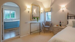 A bedroom with a bed, bedside table, chair, vanity with mirror, and a view of a bathroom. - Stream House Luxury B&B (Hastings)