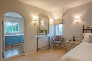 A bedroom with a bed, bedside table, chair, vanity with mirror, and a view of a bathroom.