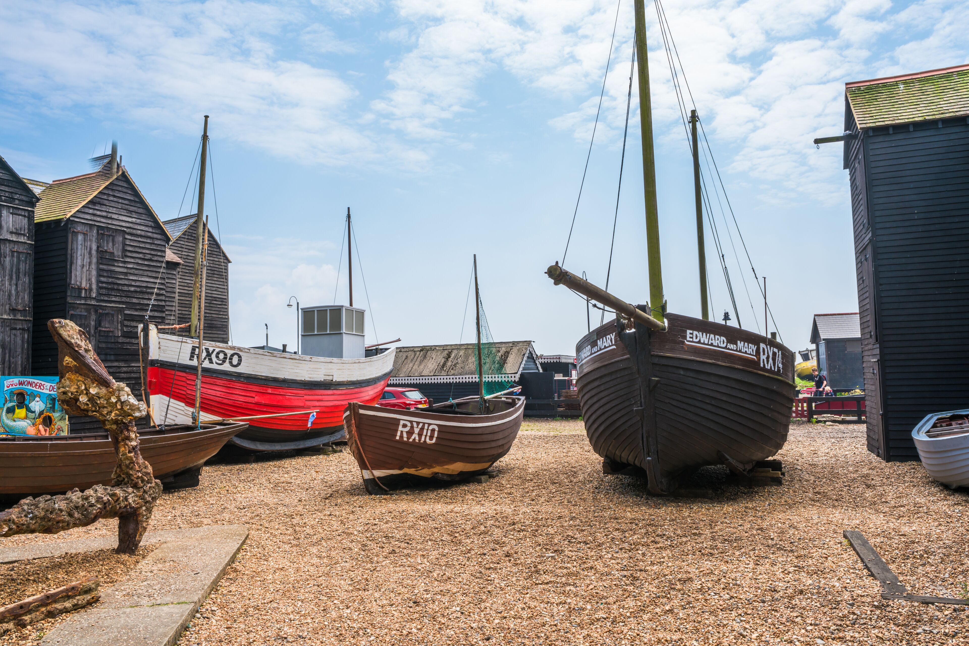 Several boats docked in a gravel area with buildings in the background.