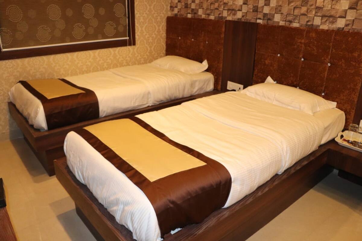 Dos camas individuales con estructuras de madera y ropa de cama blanca, un cabecero de madera y una pared con estampado.