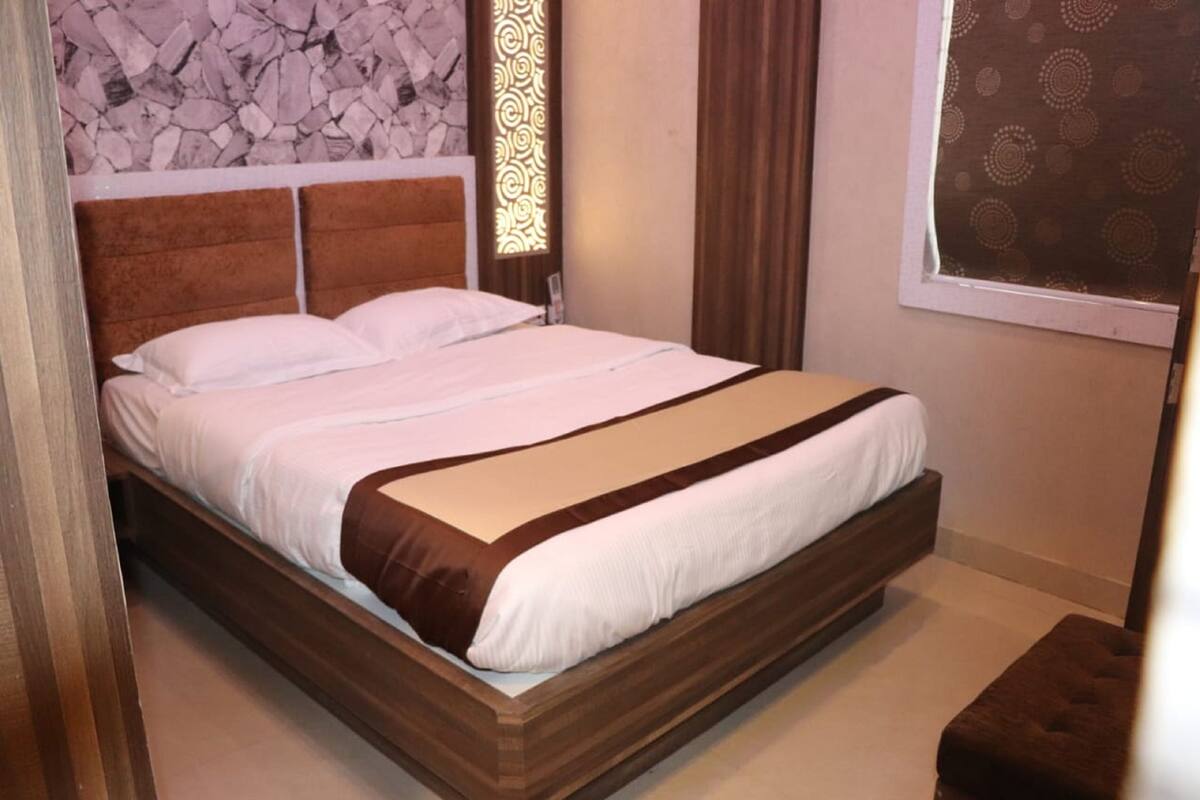 Una cama bien hecha con cabecera de madera, pared de piedra de fondo y ventana con cortinas estampadas.