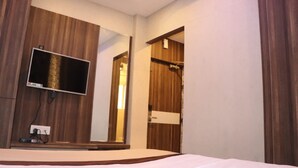 A hotel room with a bed, a TV mounted on the wall, a mirror, and a wooden wardrobe. - Hotel Angina (Kolkata)