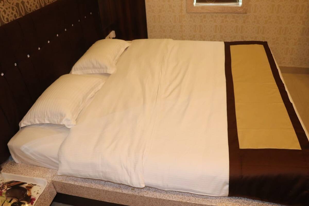 Una cama bien tendida con sábanas blancas y un detalle en tono marrón, un cabecero oscuro y una pared con estampado.