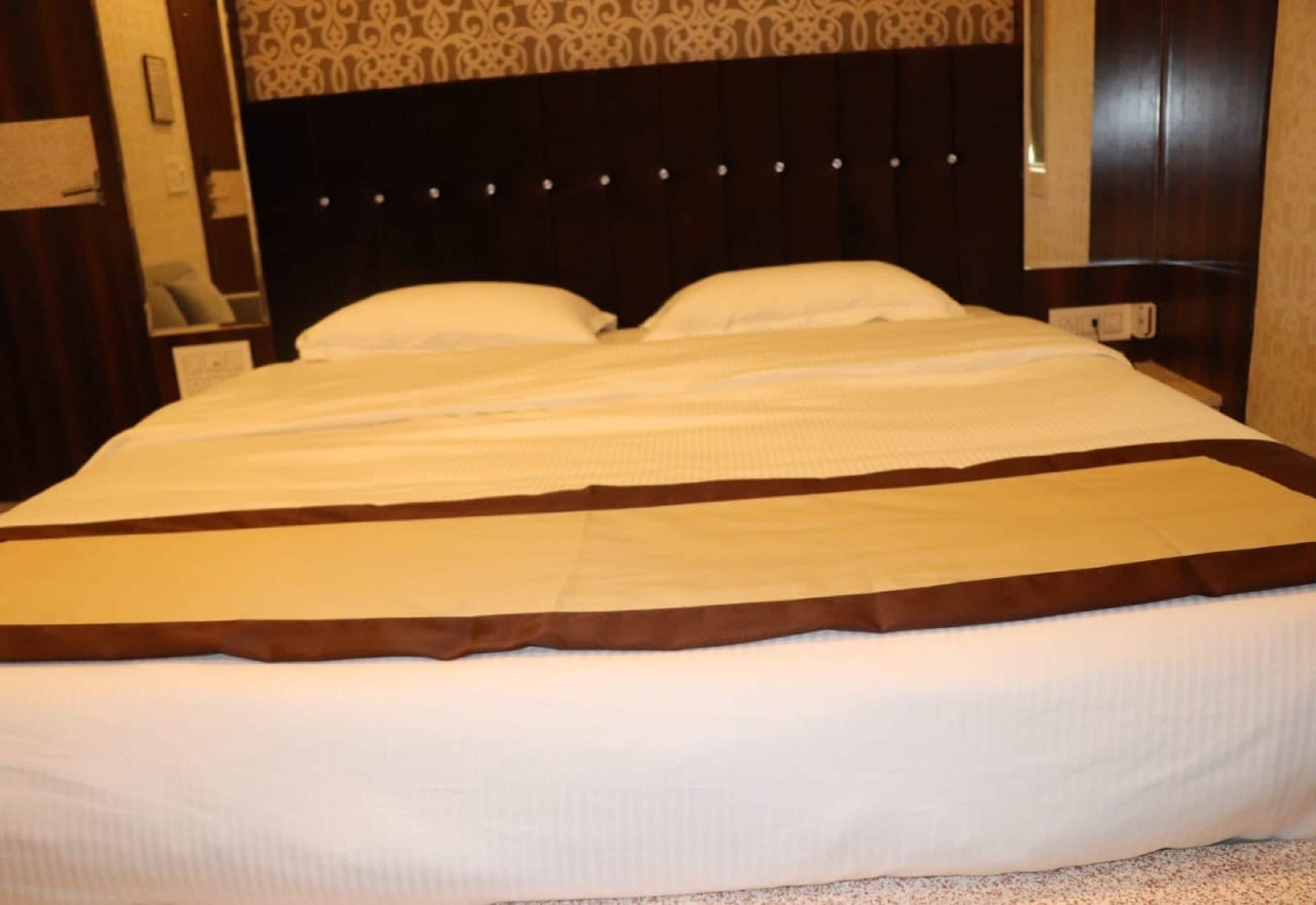 Un grand lit avec une tête de lit sombre et un mur décoré se trouve derrière.