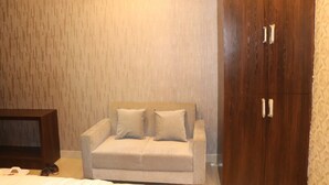 A bedroom with a wooden wardrobe, a beige sofa, and a television. - Hotel Angina (Kolkata)