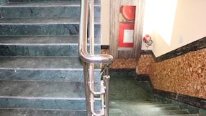 A set of stairs with a metal handrail, a fire extinguisher mounted on the wall, and a door with a red handle. - Hotel Angina (Kolkata)