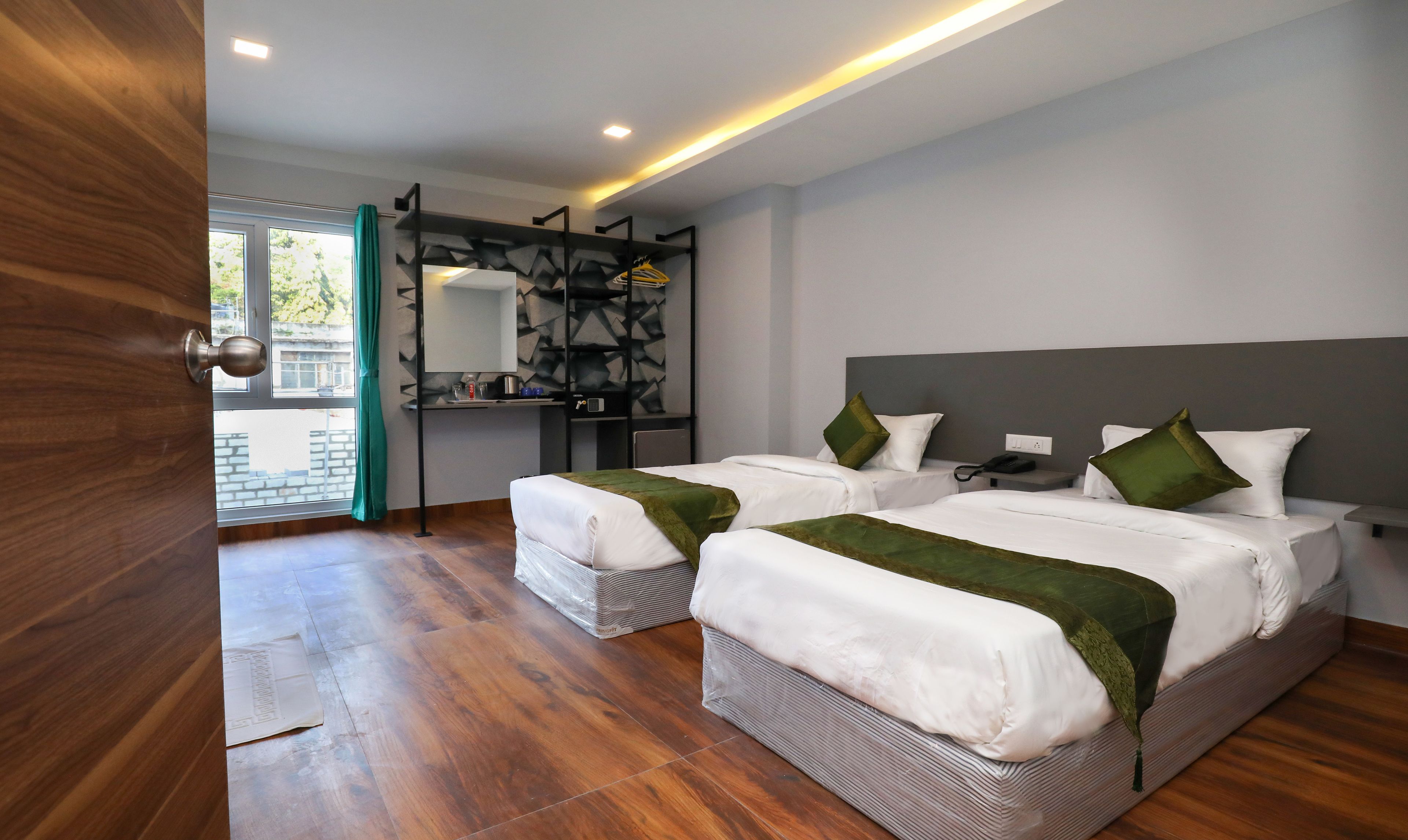 A modern hotel room with two beds, a large mirror, a small table, and a view of the outdoors.
