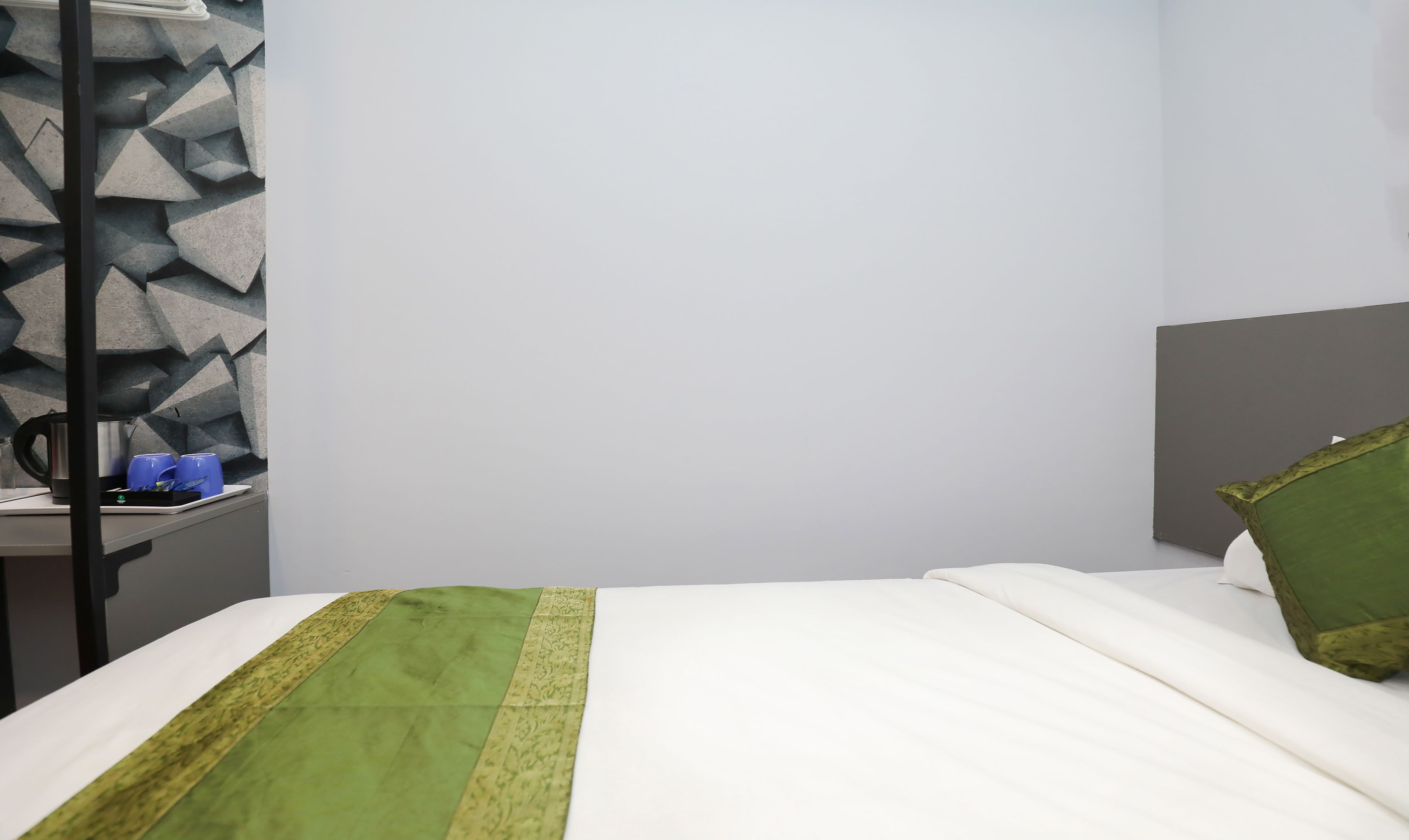 Una habitación de hotel con cama, mesita de noche, lámpara y pared con diseño geométrico.