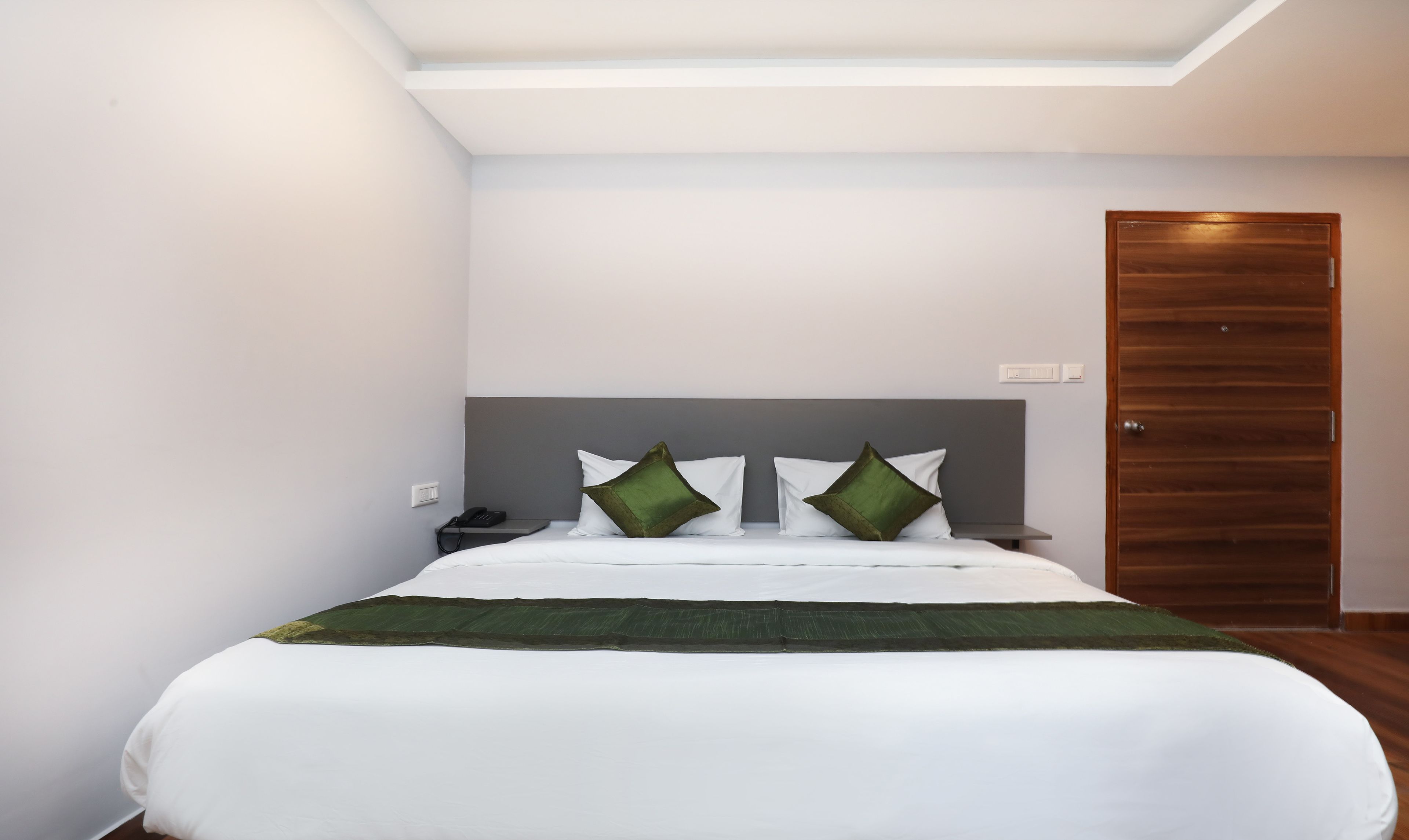 A modern hotel room with a large bed, a wooden door, and a skylight.