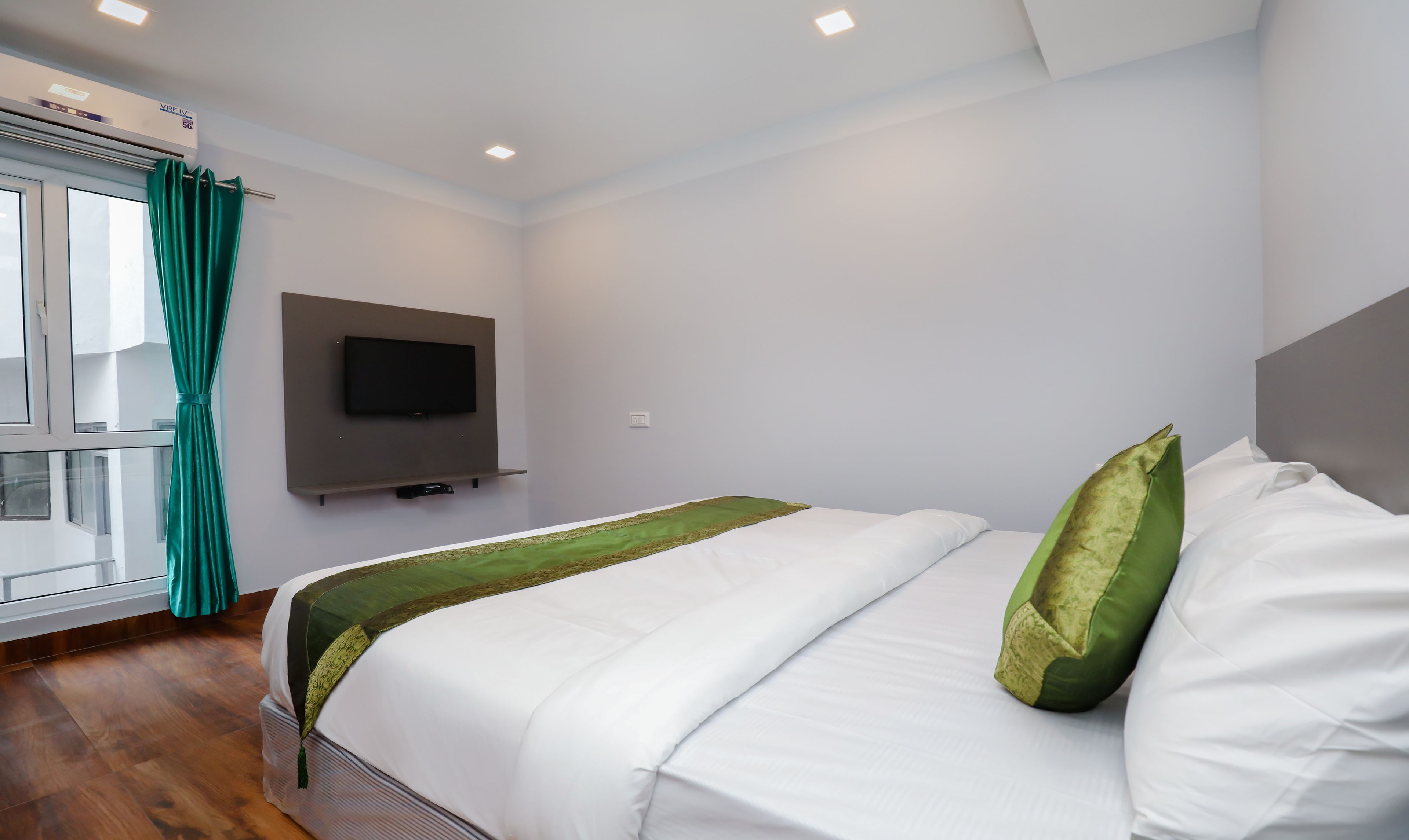 A hotel room with a bed, a TV mounted on the wall, and a window with curtains.