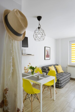 Una sala de estar moderna con un sofá blanco, sillas amarillas, una mesa de comedor y un sombrero sobre una cortina.