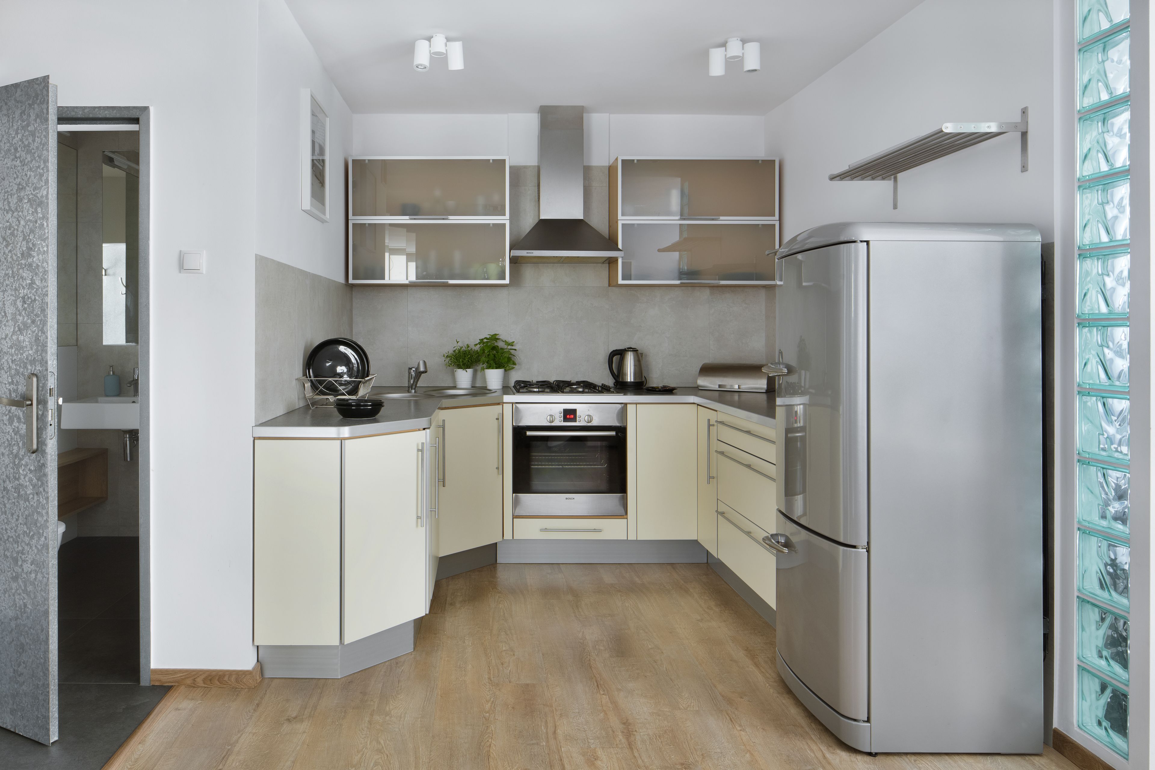 A compact kitchen with a built-in oven, a stainless steel refrigerator, and a small countertop with a kettle and a plant.