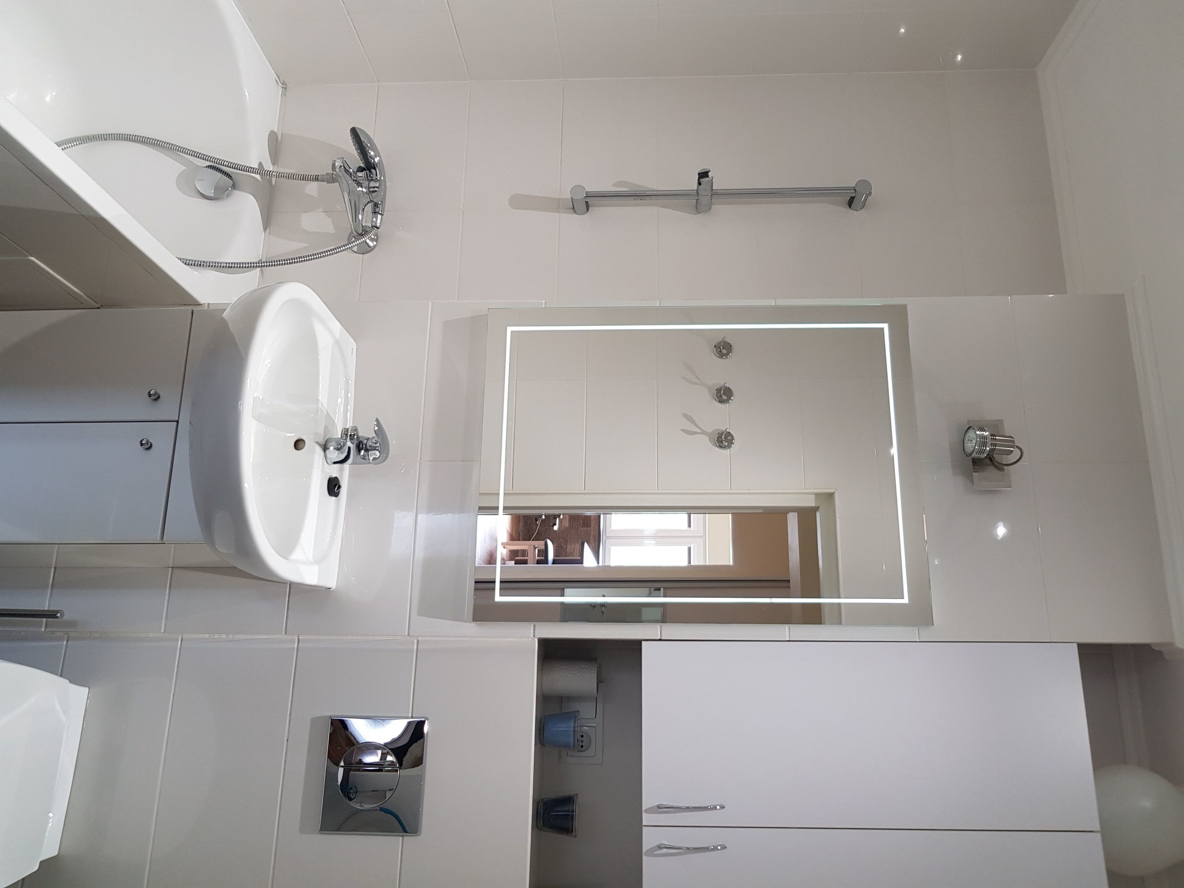 A modern bathroom with a large mirror, a bathtub, and a toilet.