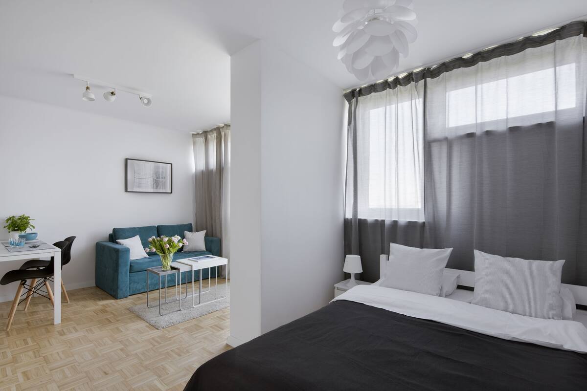 A modern hotel room with a large bed, a sofa, a small table with a plant, and a desk with a chair.