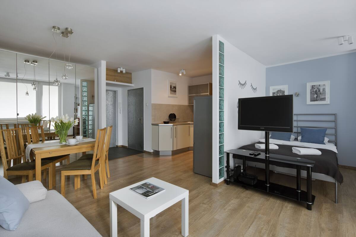 A modern living room with a dining area, a kitchen, and a bedroom with a TV.