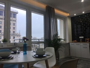 Un comedor moderno con una mesa redonda, sillas y vistas a un paisaje urbano a través de amplios ventanales.