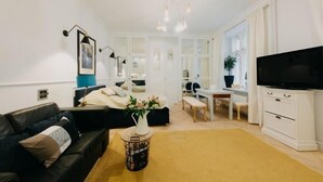 Un salon moderne avec un canapé en cuir noir, un meuble TV blanc et un coin repas comprenant une table et des chaises.