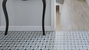 Une chambre moderne avec un grand miroir noir à motifs, une orchidée en pot et une chaise blanche.
