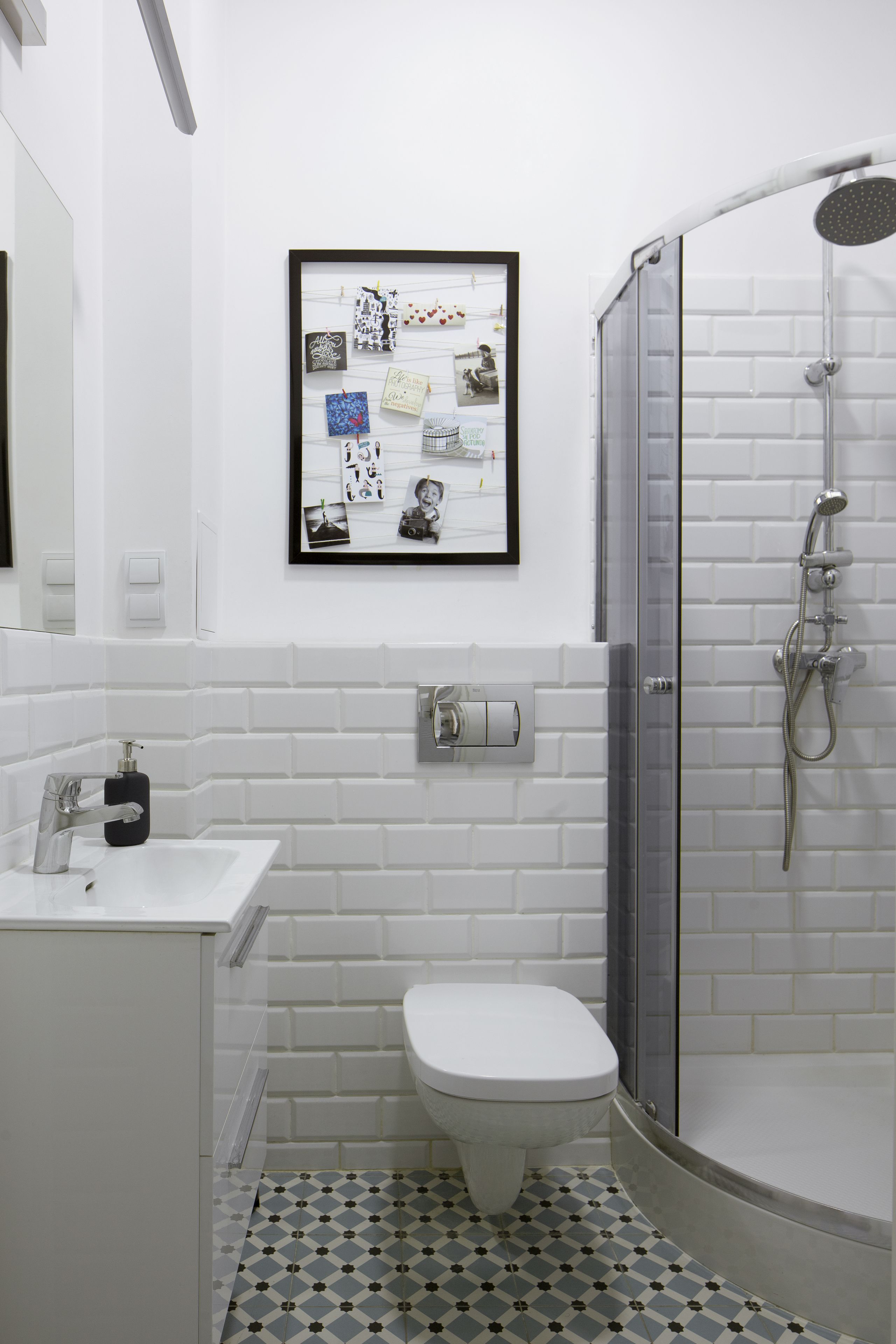 A bathroom with a white toilet, a sink, a shower with a glass door, and a framed collage on the wall.
