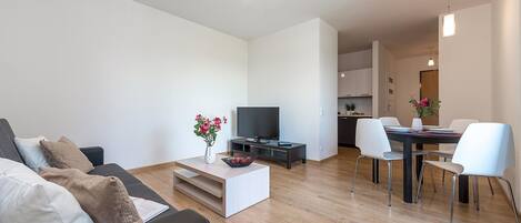 A modern living room with a sofa, coffee table, TV, and dining area.