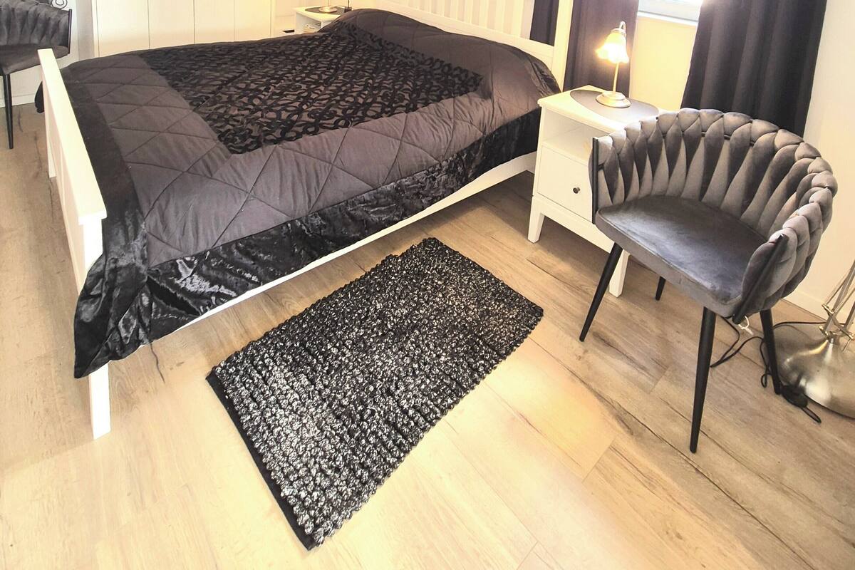 A bedroom with a bed, a chair, a desk, a lamp, a ceiling fan, and a window with curtains.