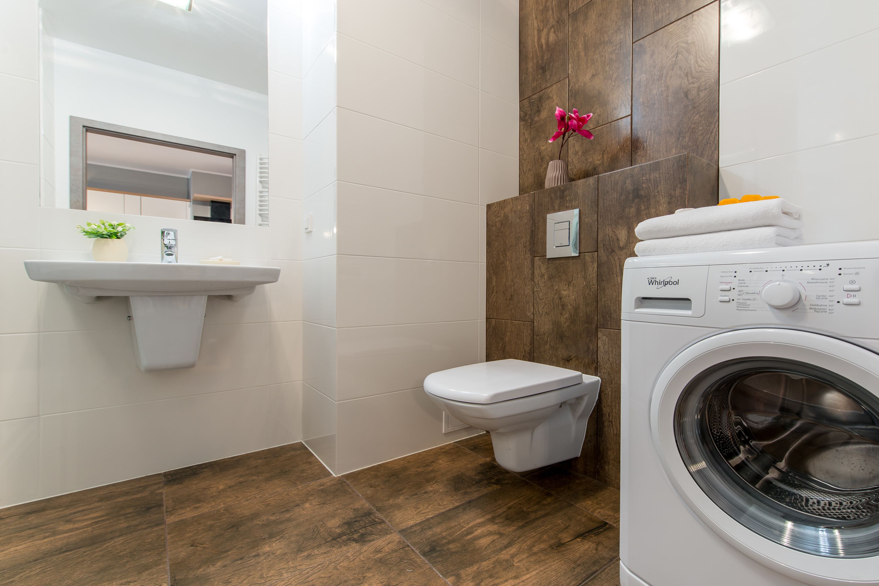 A modern bathroom with a white sink, toilet, and a front-loading washing machine.