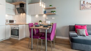 A modern kitchen with white cabinets, a built-in oven, and a dining area with purple chairs.