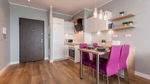 A modern kitchen with white cabinets, a dark door, and a dining area with purple chairs.