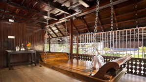 A wooden bench with a white cloth, a table with a vase, and a view through a lattice window. - Spices Lap Thekkady (Udumbanchola)