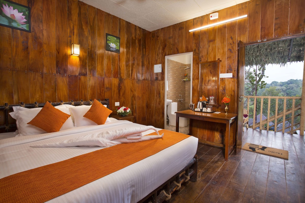 Quarto com decoração em madeira, com cama, almofadas, mesa de cabeceira e vista para o exterior.