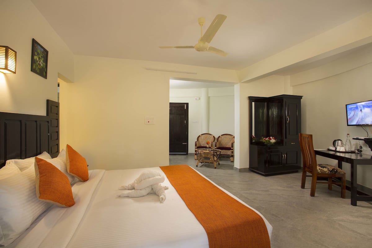 Quarto de hotel com cama, secretária, televisão e área de jantar com cadeiras.