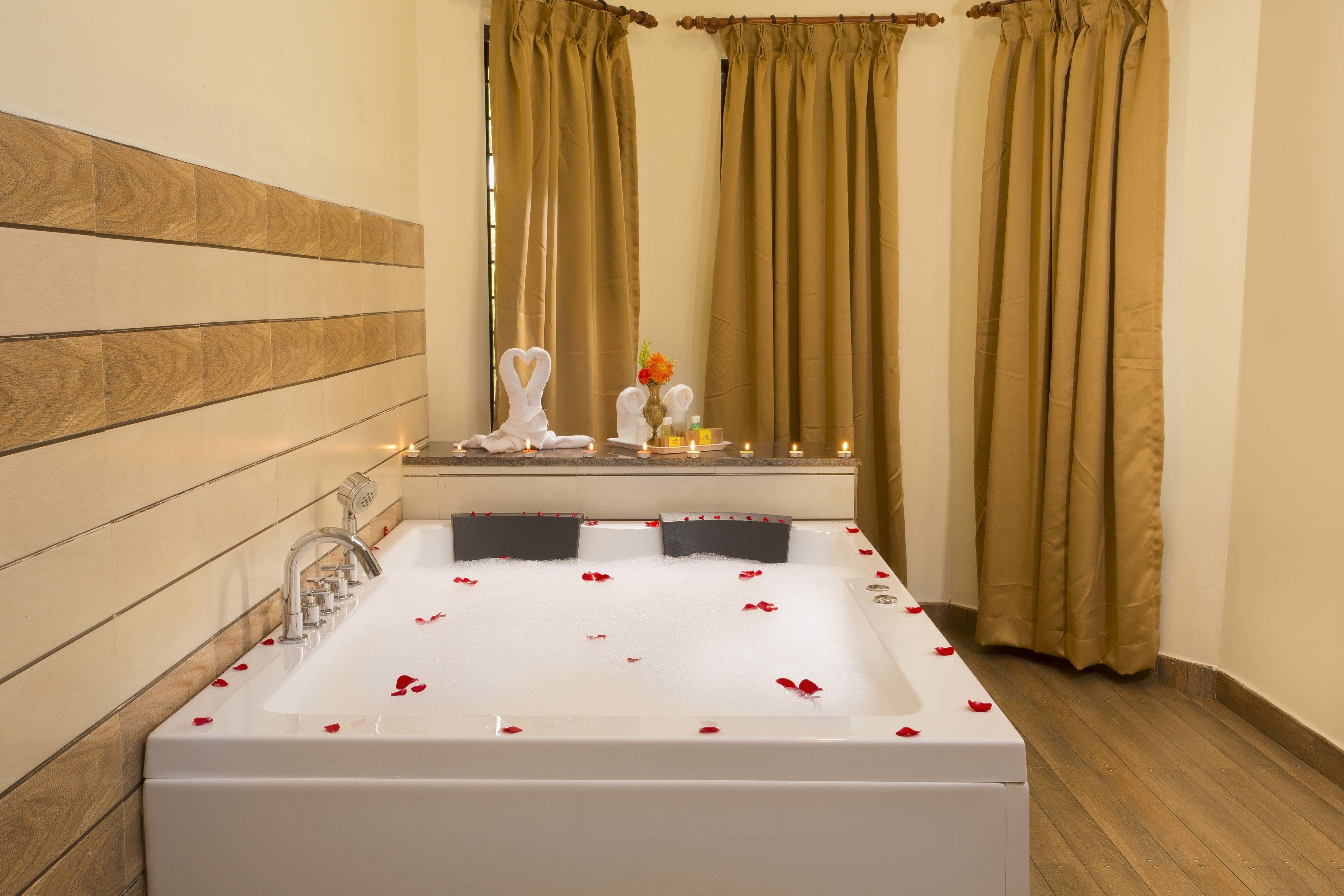 A bathroom with a large bathtub, wooden paneling on the wall, and a window with curtains.
