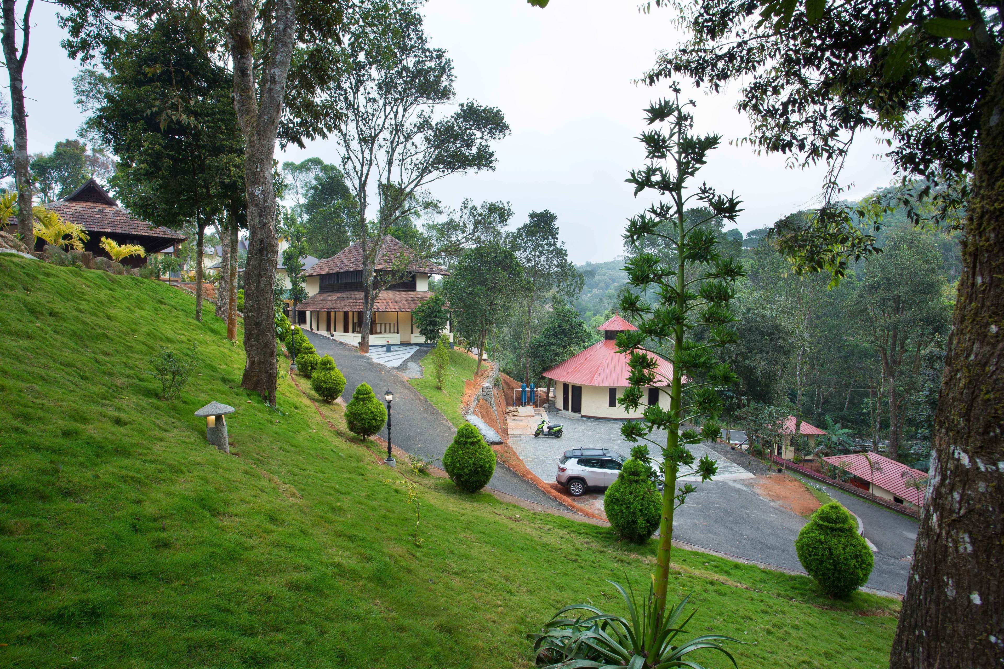A hillside residential area with houses, a paved road, and lush greenery.
