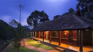 A traditional wooden building with a tiled roof, surrounded by a well-maintained garden and a pathway leading to the entrance. - Spices Lap Thekkady (Udumbanchola)
