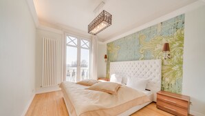 A bedroom with a large bed, a nightstand, a dresser, a radiator, and a window with curtains. - Villa Rhenus (Ginsheim-Gustavsburg)
