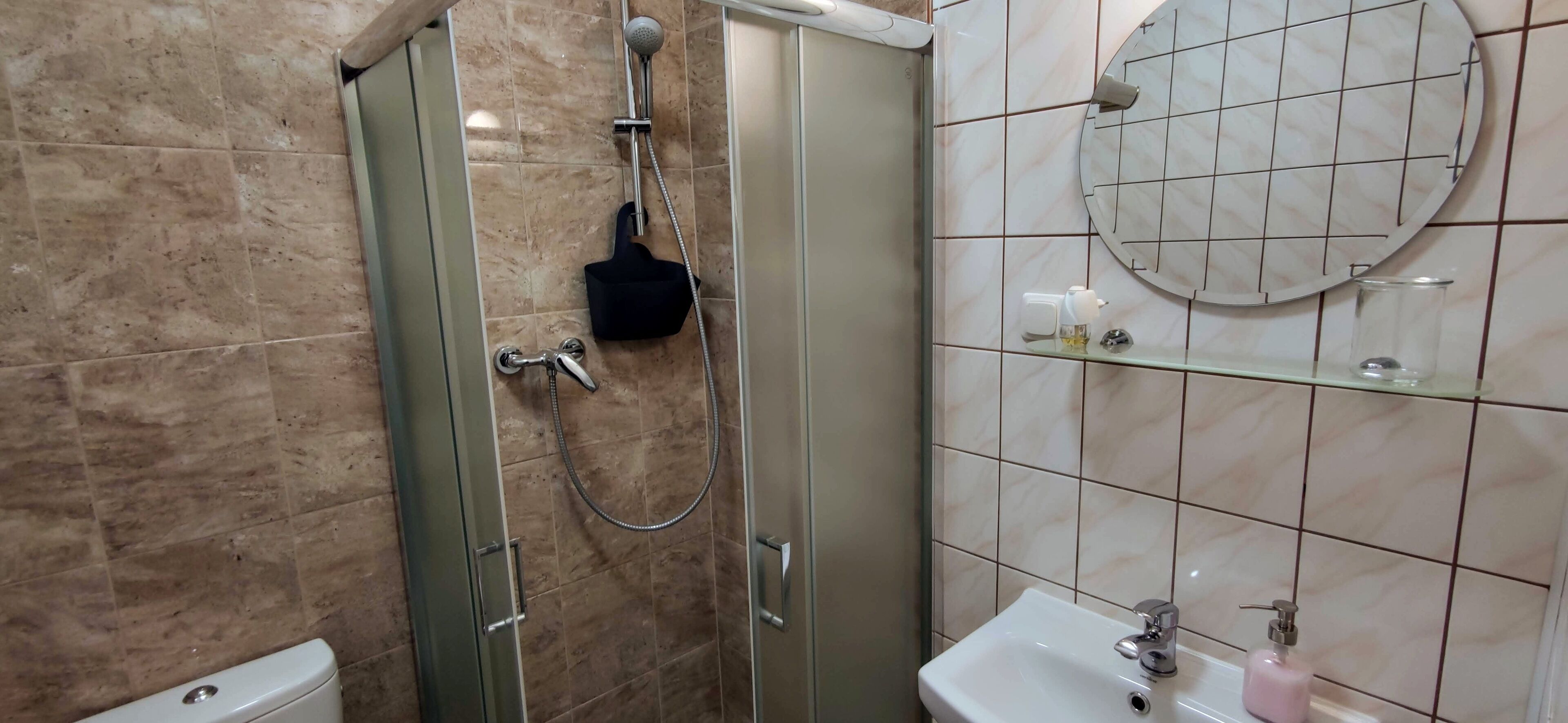 A bathroom with a glass-enclosed shower, a sink with a mirror, and a shelf with toiletries.