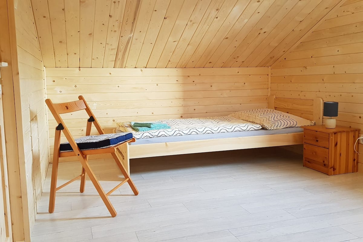 A small, wooden-paneled room with a single bed, a wooden chair, and a bedside table with a lamp.