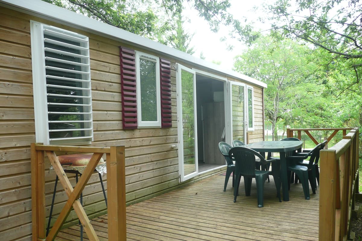 Une terrasse en bois avec une table et des chaises, une porte-fenêtre coulissante et une vue sur une zone boisée.