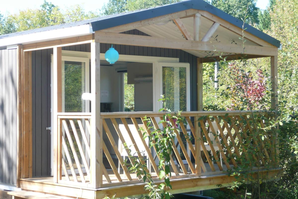 Une cabane en bois dotée d’un balcon, de grandes fenêtres et d’une véranda couverte.