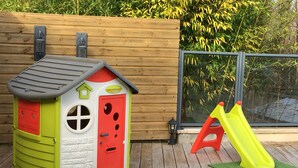Casa de juegos infantil con un tobogán y un camión volquete de juguete sobre una terraza de madera.