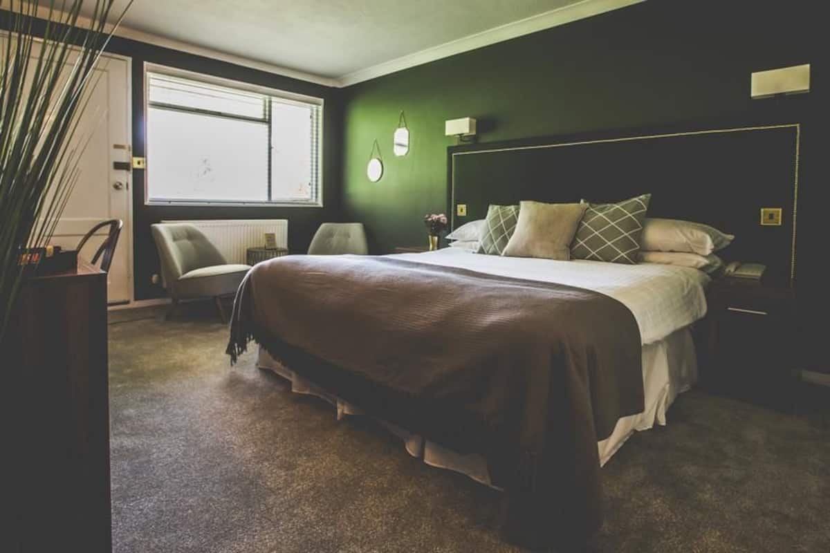 Quarto com cama grande, uma cadeira, escrivaninha e janela.