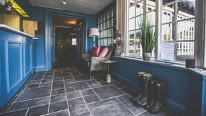 Een gang met een blauwe wand, een stoel met roze kussens, een lamp en een raam met uitzicht op gebouwen.
