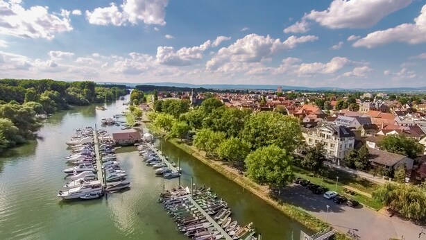 A riverside town with a marina, historic buildings, and a prominent church tower. - Apartmenthaus am Rhein (Ginsheim-Gustavsburg)