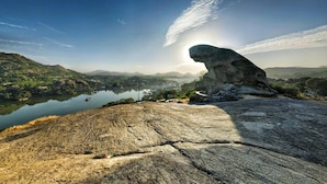 A rocky landscape with a large boulder, a lake, and distant mountains. - Eminence - Palm Residency (Abu Road)