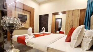 A hotel room with a bed, a television, a wooden wardrobe, and a ceiling fan. - Eminence - Palm Residency (Abu Road)