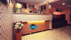 A reception desk with a wooden finish, a logo, and a vase of flowers. - Eminence - Palm Residency (Abu Road)