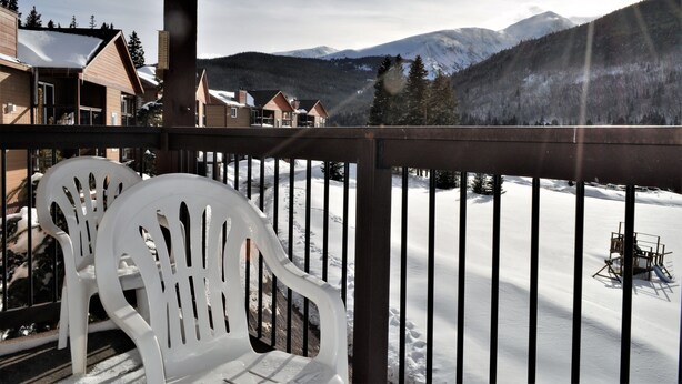 A wooden deck with white plastic chairs, overlooking a snow-covered landscape with mountains and trees. - Blue River Condos 3 Bed 2 Bath (Breckenridge)