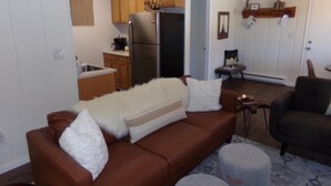 A living room with a brown sofa, a white fluffy blanket, and a grey ottoman. - Blue River Condos 3 Bed 2 Bath (Breckenridge)