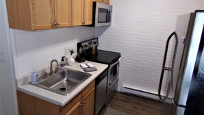 A compact kitchen with wooden cabinets, a stainless steel sink, a microwave, a stove, and a refrigerator. - Blue River Condos 3 Bed 2 Bath (Breckenridge)